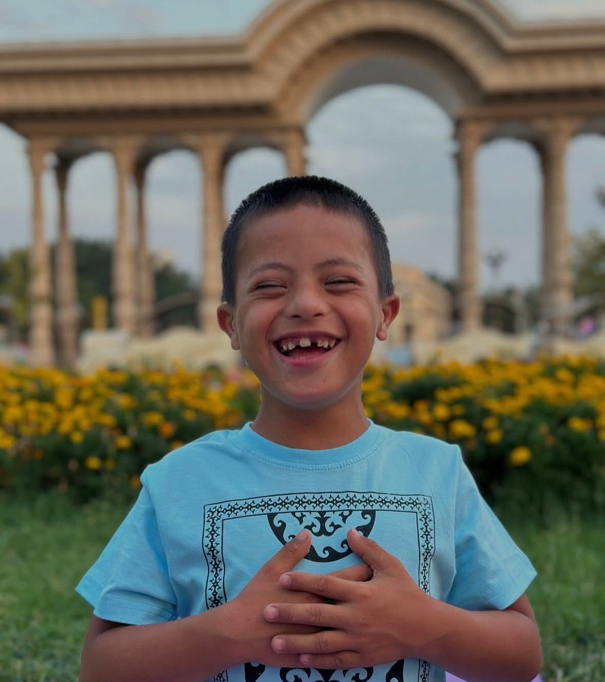 A boy with Down syndrome laughing with his hands on his chest, in a park in Tajikistan